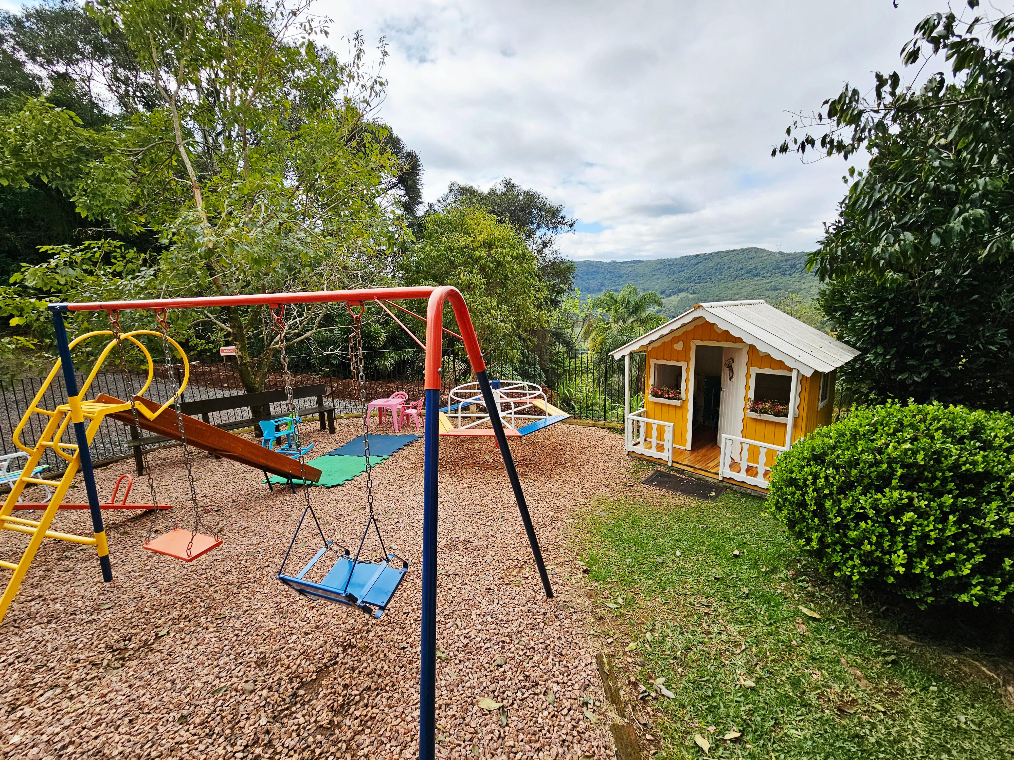 Parquinho da área kids com balanços, escorregador e casinha amarela com vista para a serra