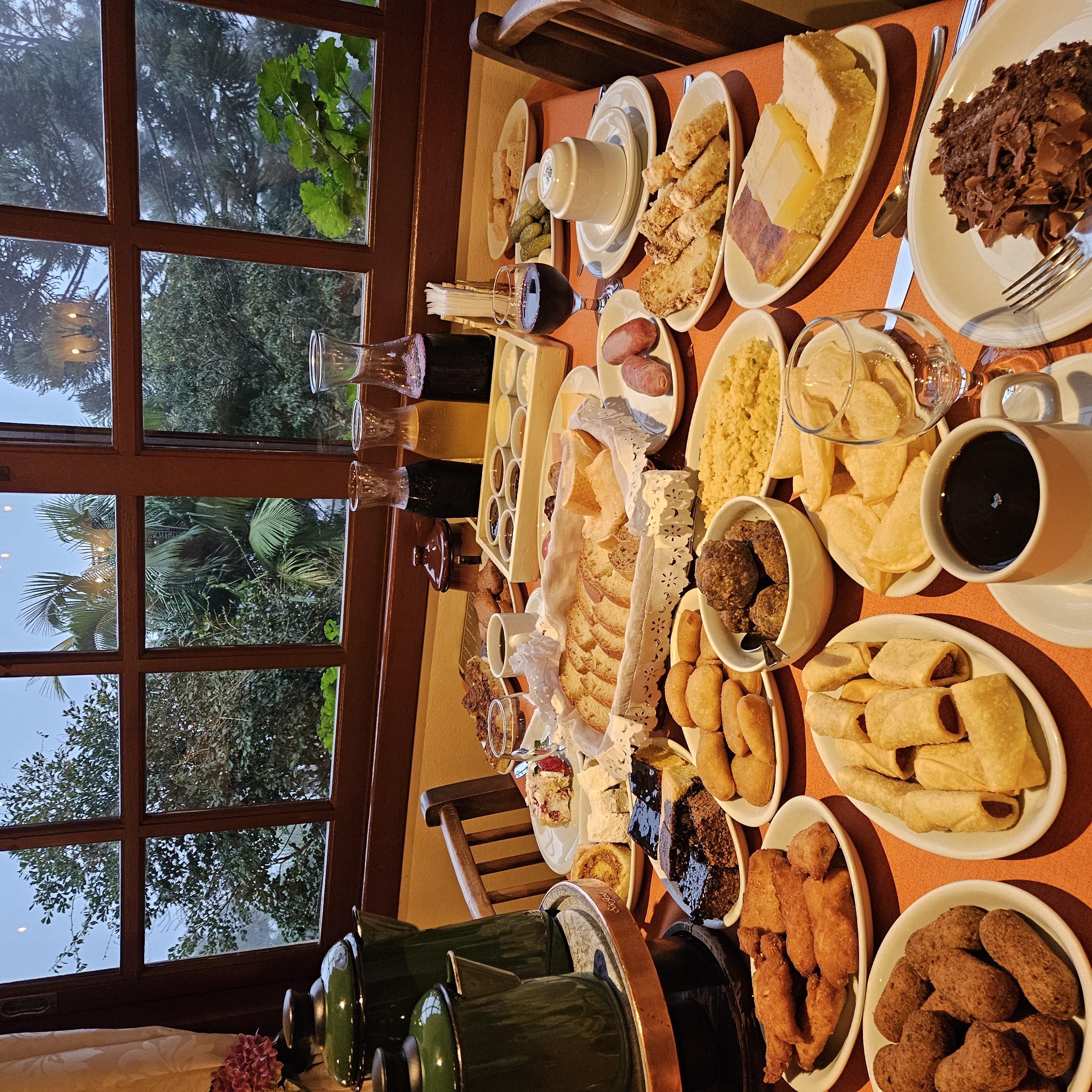 Mesa farta do Café Colonial Walachay com vista pela janela colonial para a vegetação da Serra Gaúcha